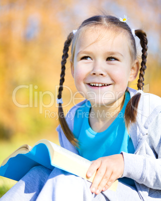 Little girl is reading a book outdoors