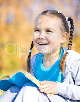 Little girl is reading a book outdoors