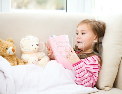 Little girl is reading a book for her teddy bears
