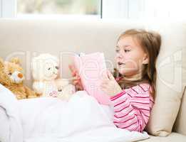 Little girl is reading a book for her teddy bears