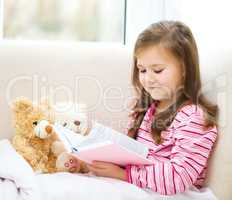 Little girl is reading a story for her teddy bears