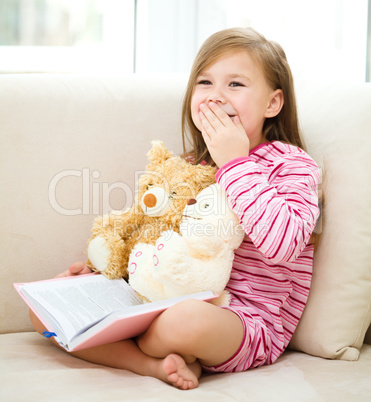 Little girl is reading a book for her teddy bears