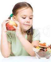 Little girl choosing between apples and sweets