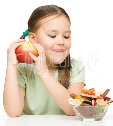 Little girl choosing between apples and sweets