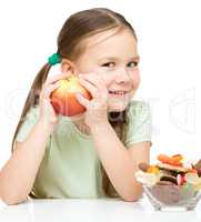 Little girl choosing between apples and sweets