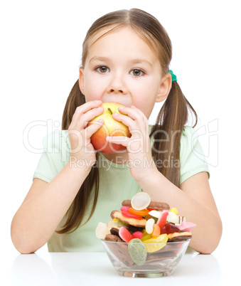 Little girl choosing between apples and sweets