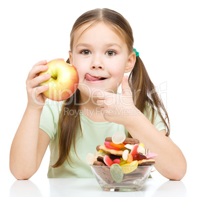 Little girl choosing between apples and sweets