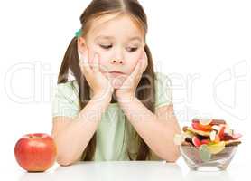 Little girl choosing between apples and sweets