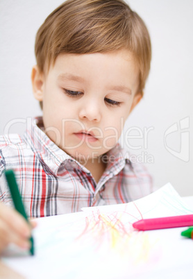 Little boy is drawing on white paper