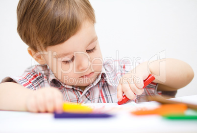 Little boy is drawing on white paper