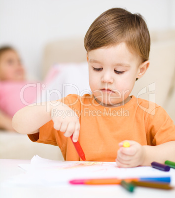 Little boy is drawing on white paper