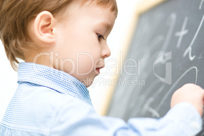 Little boy is writing on blackboard
