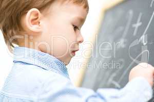 Little boy is writing on blackboard