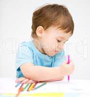 Little boy is drawing on white paper