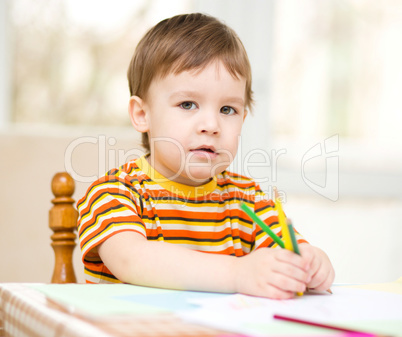 Little boy is drawing on white paper