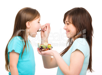 Mother is feeding her daughter with fruit salad