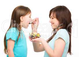 Mother is feeding her daughter with fruit salad
