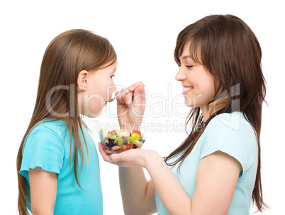 Mother is feeding her daughter with fruit salad