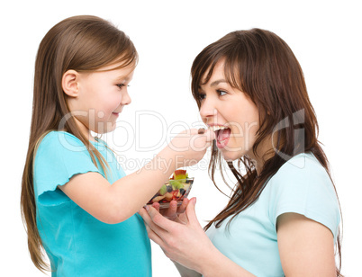 Daughter is feeding her mother with fruit salad