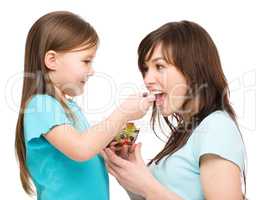 Daughter is feeding her mother with fruit salad