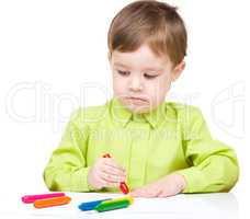 Little boy is drawing on white paper using crayon