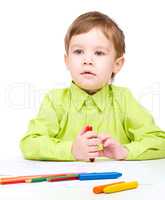 Little boy is drawing on white paper using crayon