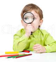 Cute little boy is playing with magnifier