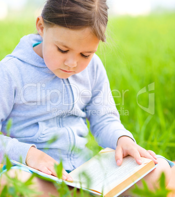 Little girl is reading a book outdoors