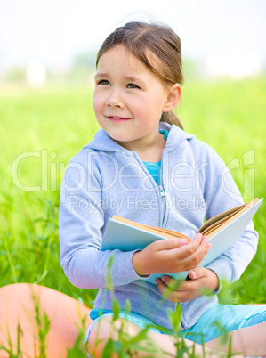 Little girl is reading a book outdoors