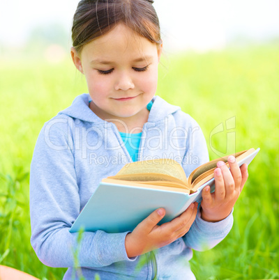 Little girl is reading a book outdoors