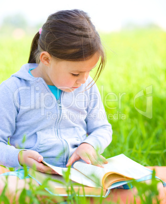 Little girl is reading a book outdoors