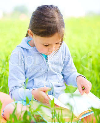 Little girl is reading a book outdoors