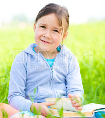 Little girl is reading a book outdoors