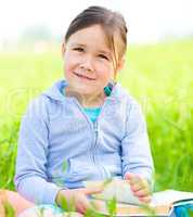 Little girl is reading a book outdoors