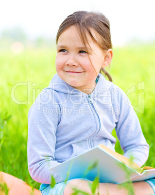 Little girl is reading a book outdoors