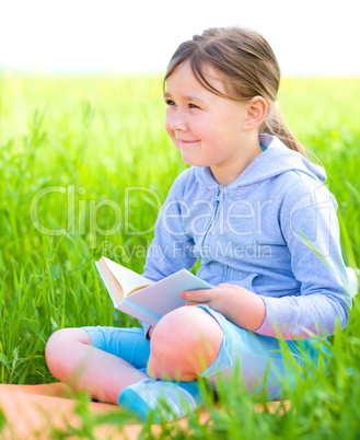 Little girl is reading a book outdoors