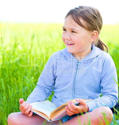 Little girl is reading a book outdoors