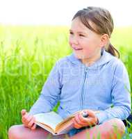 Little girl is reading a book outdoors