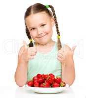 Happy little girl is eating strawberries