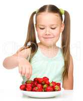 Happy little girl is eating strawberries