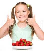 Happy little girl is eating strawberries