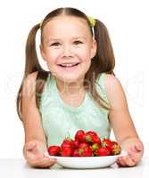 Cheerful little girl is eating strawberries