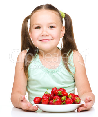 Cheerful little girl is eating strawberries