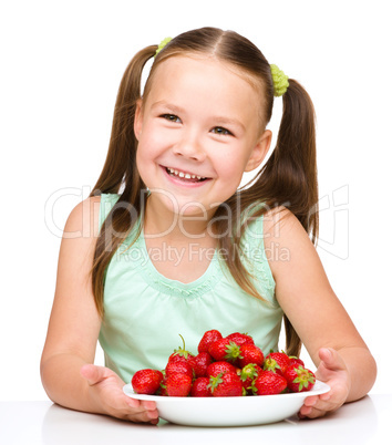 Cheerful little girl is eating strawberries
