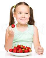 Cheerful little girl is eating strawberries