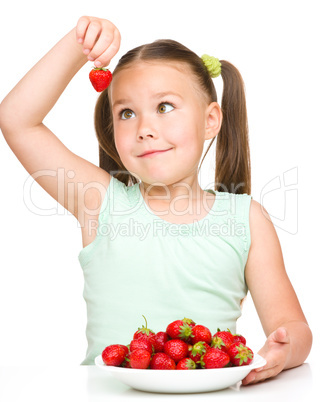 Cheerful little girl is eating strawberries