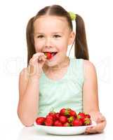 Happy little girl is eating strawberries