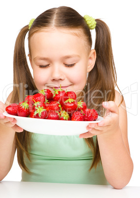 Cheerful little girl is smelling strawberries