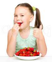 Happy little girl is eating strawberries