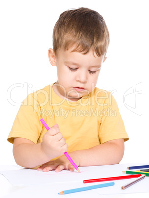 Little boy is drawing using color pencils